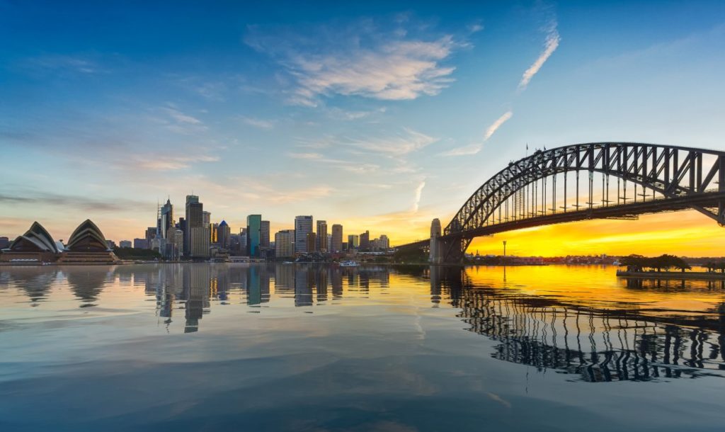 Dramatic widescreen panoramic image of the city of Sydney at sunset including the Rocks, Bridge and Opera House with an artificial reflection for the ocean